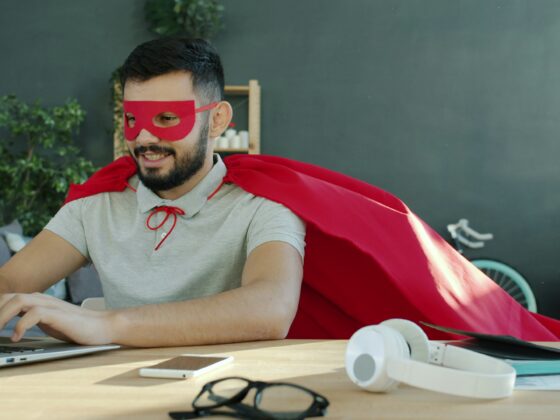 A man wearing a superhero costume and typing on a laptop.