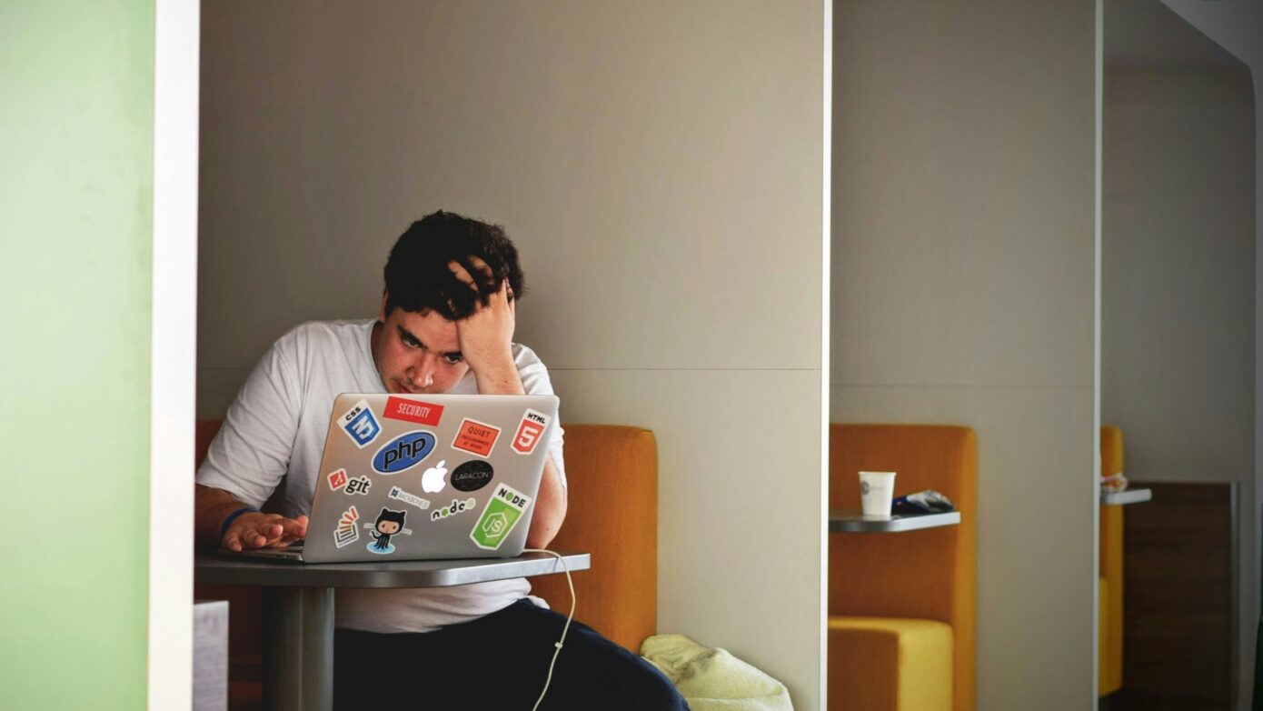 A man holding his head in frustration while working on a laptop.