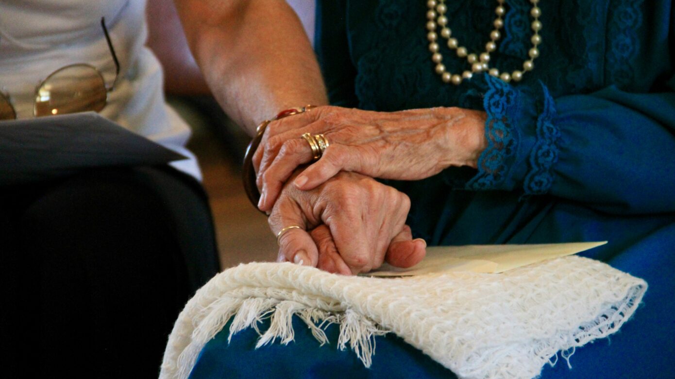 A close-up of two people holding hands, with one pair of hands appearing to be those of an elderly woman.