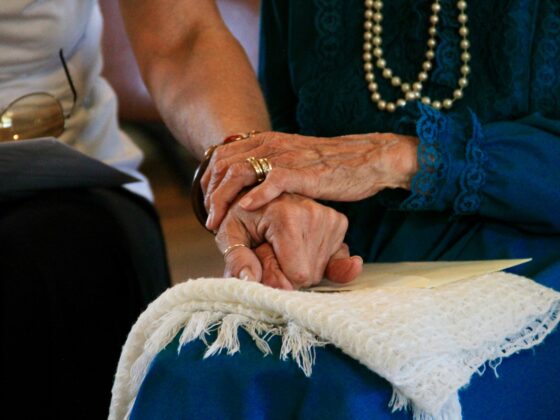 A close-up of two people holding hands, with one pair of hands appearing to be those of an elderly woman.