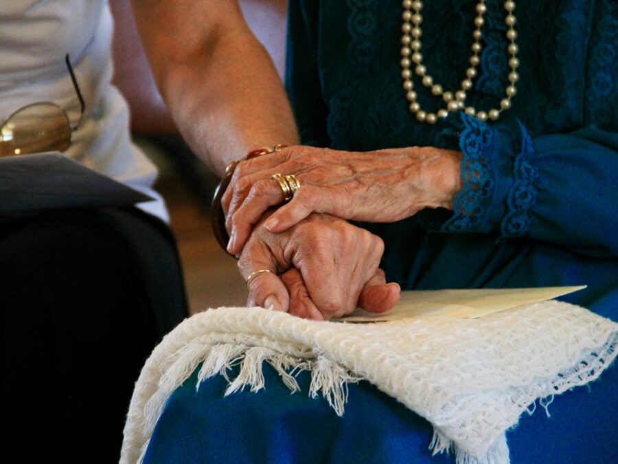 A close-up of two people holding hands, with one pair of hands appearing to be those of an elderly woman.
