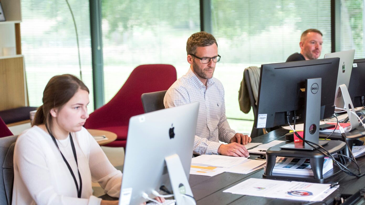 Three workers at their desks, working on computers.