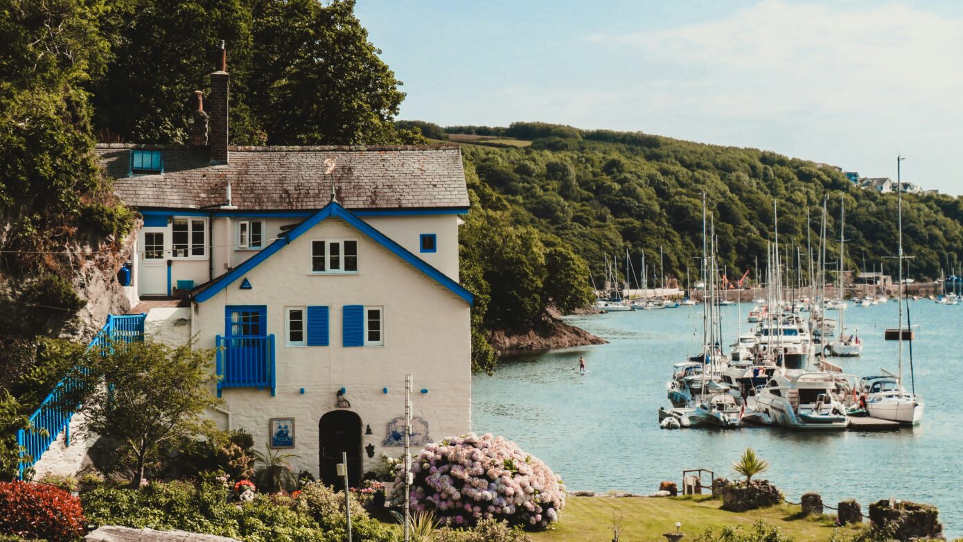 A house with clue shutters next to boats on the water.
