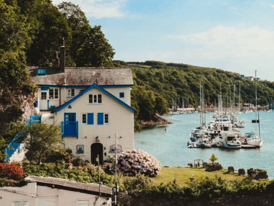 A house with clue shutters next to boats on the water.