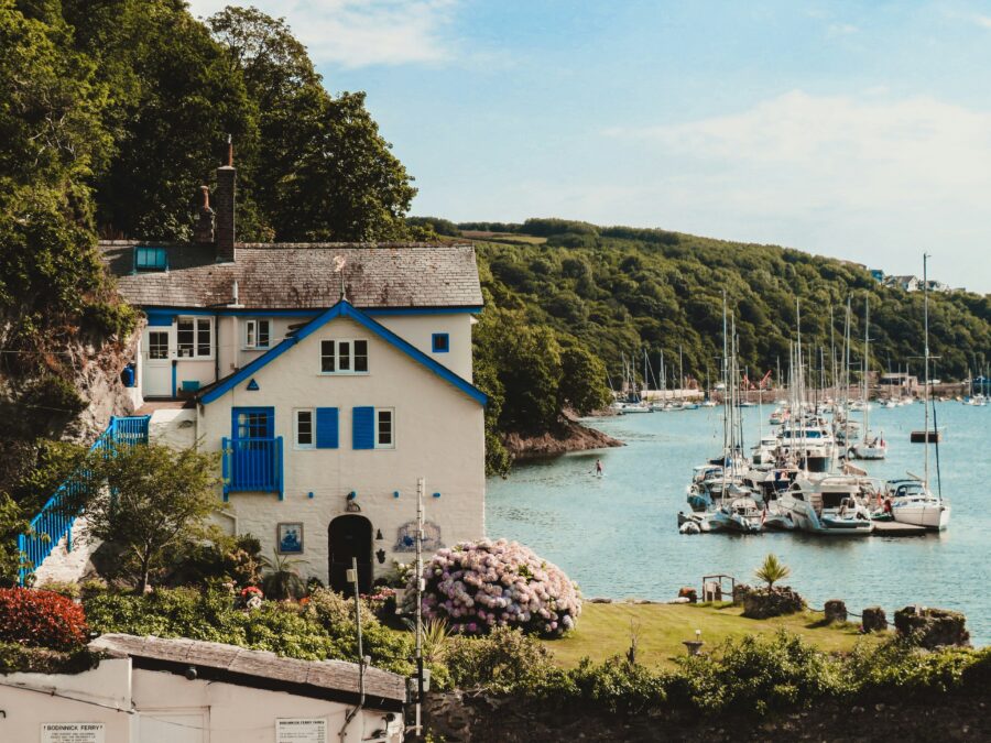 A house with clue shutters next to boats on the water.